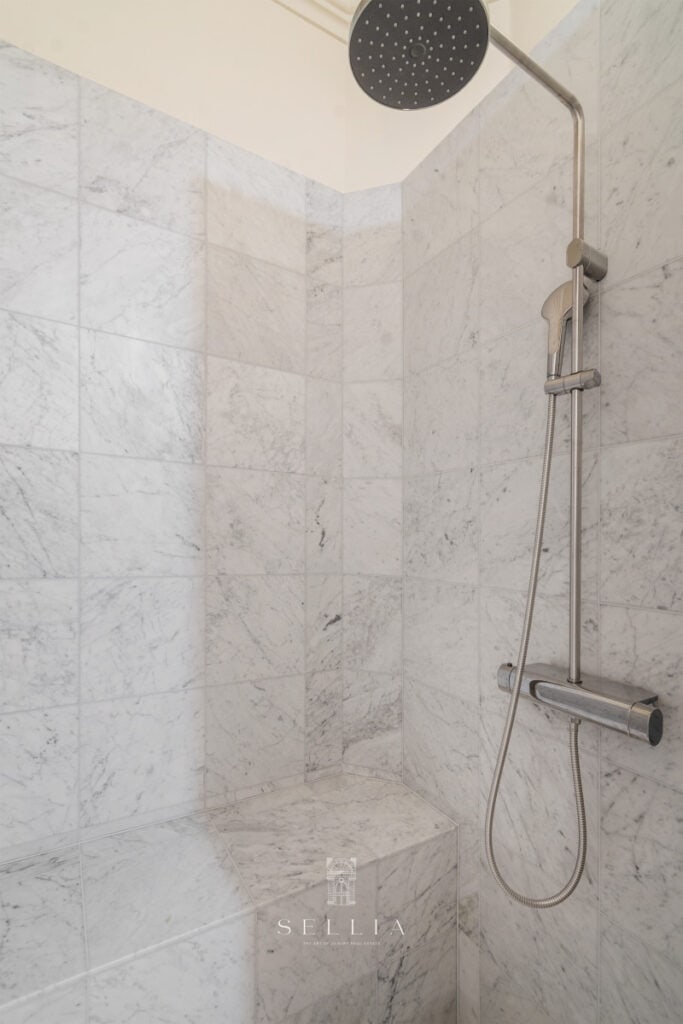 Przytulna łazienka z marmurowymi ścianami i funkcjonalnym deszczownicą.