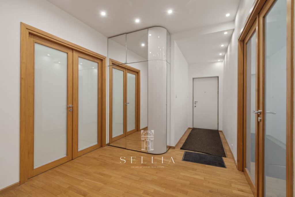 Przestronne wejście do mieszkania z dużymi drewnianymi drzwiami i jasną ścianą, idealne do aranżacji.