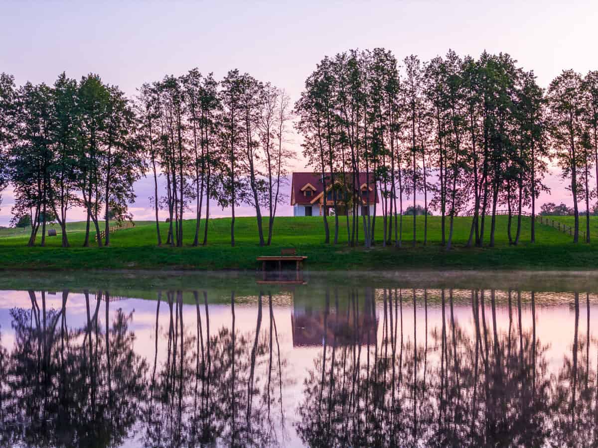 Luksowna rezydencja nad jeziorem z widokiem na wodę i drzewa o zachodzie słońca.