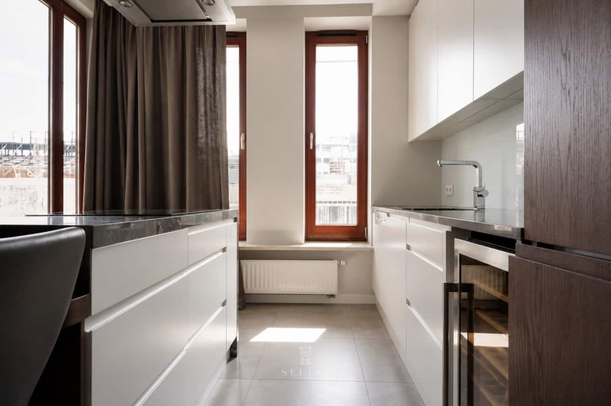 Nowoczesna kuchnia z dużymi oknami i białymi szafkami w apartamencie na Powiślu.