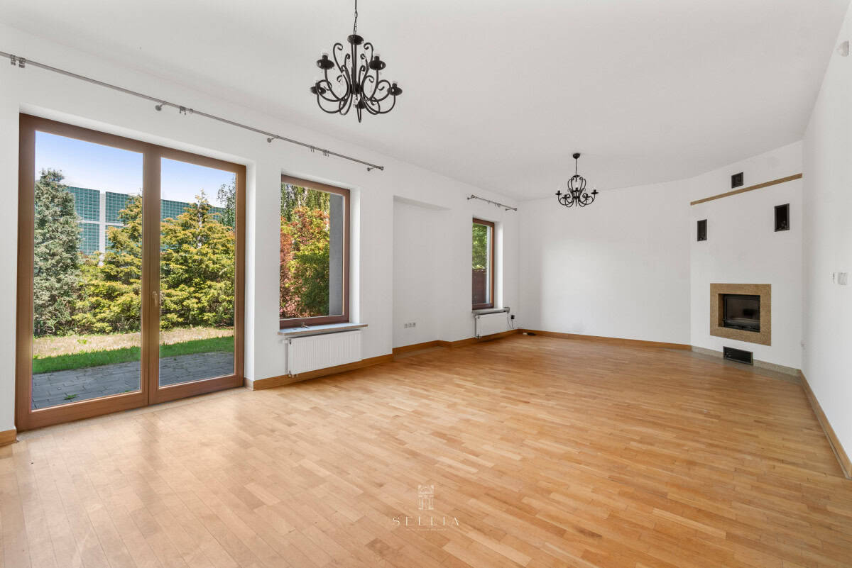 Przestronny salon z dużymi oknami i kominkiem w nowoczesnym domu na Wilanowie.