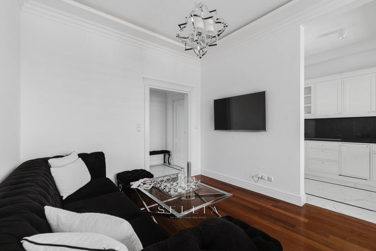 Nowoczesny salon z telewizorem i czarną sofą w eleganckim apartamencie.