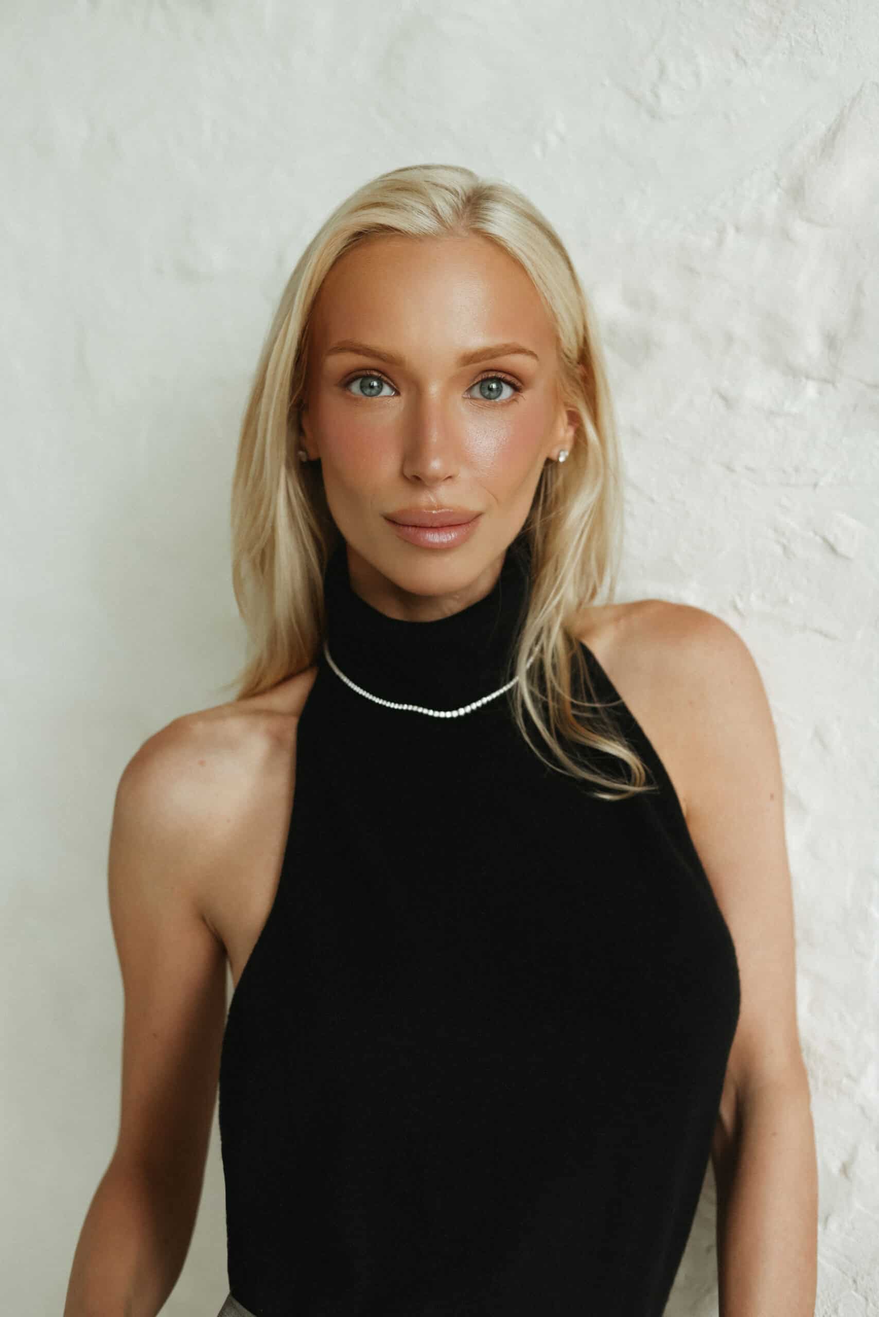 Portret eleganckiej kobiety w czarnym topie przy białej ścianie.