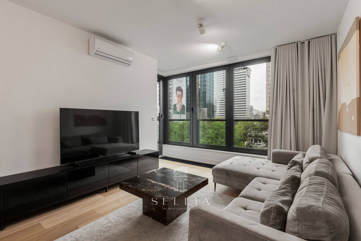 Nowoczesny salon z dużymi oknami i balkonem w apartamencie na wynajem.